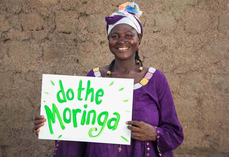 Woman holding a sign that says "do the Moringa"