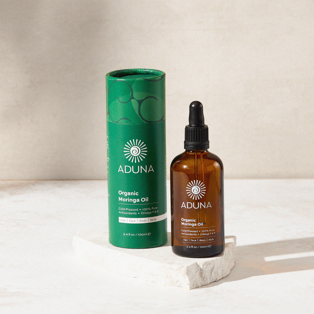 Aduna Moringa Beauty Oil - Tub & Bottle displayed on marble stand