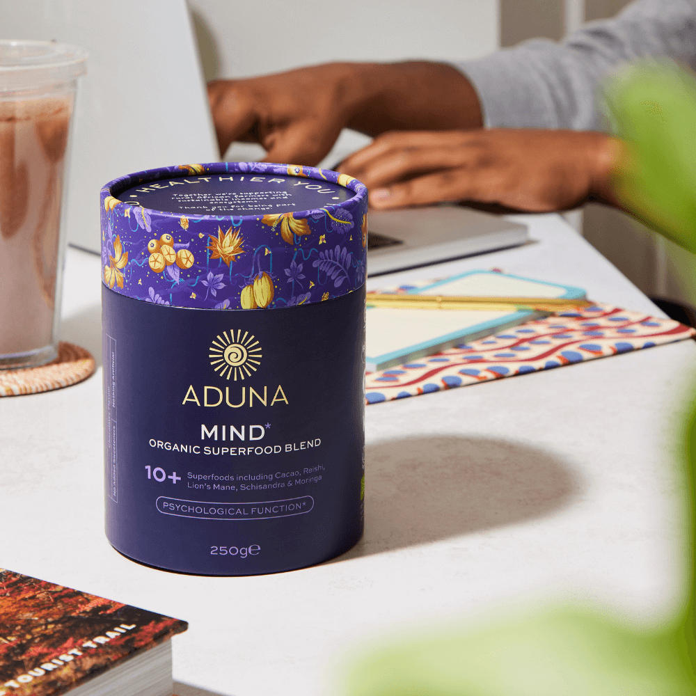 Aduna Mind Organic Superfood Blend 250g package next to someone working on a laptop.