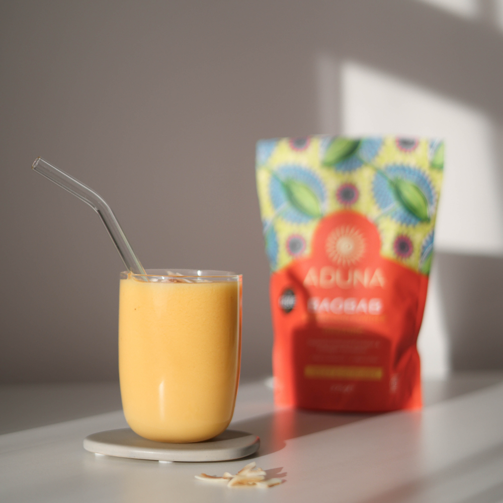 Aduna Baobab Powder pack stood next to an orange-coloured juice in a glass.