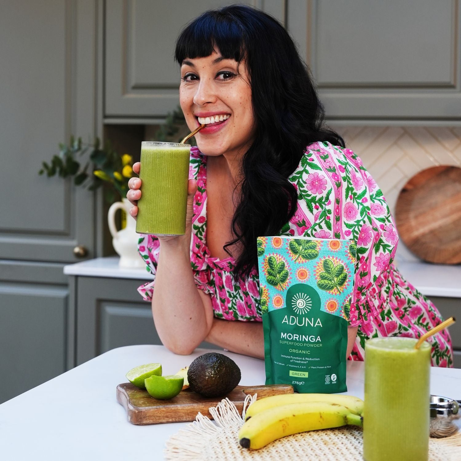 Melissa Hemsley enjoying a green smoothie with Aduna Moringa packaging in a kitchen setting.