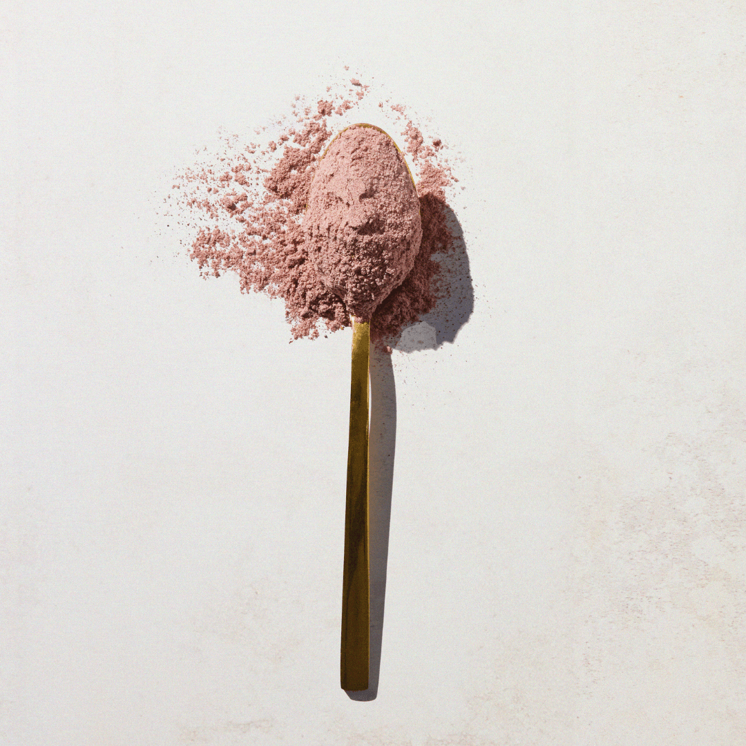 A gold spoon filled with light pink Aduna Beauty Superfood Blend Powder