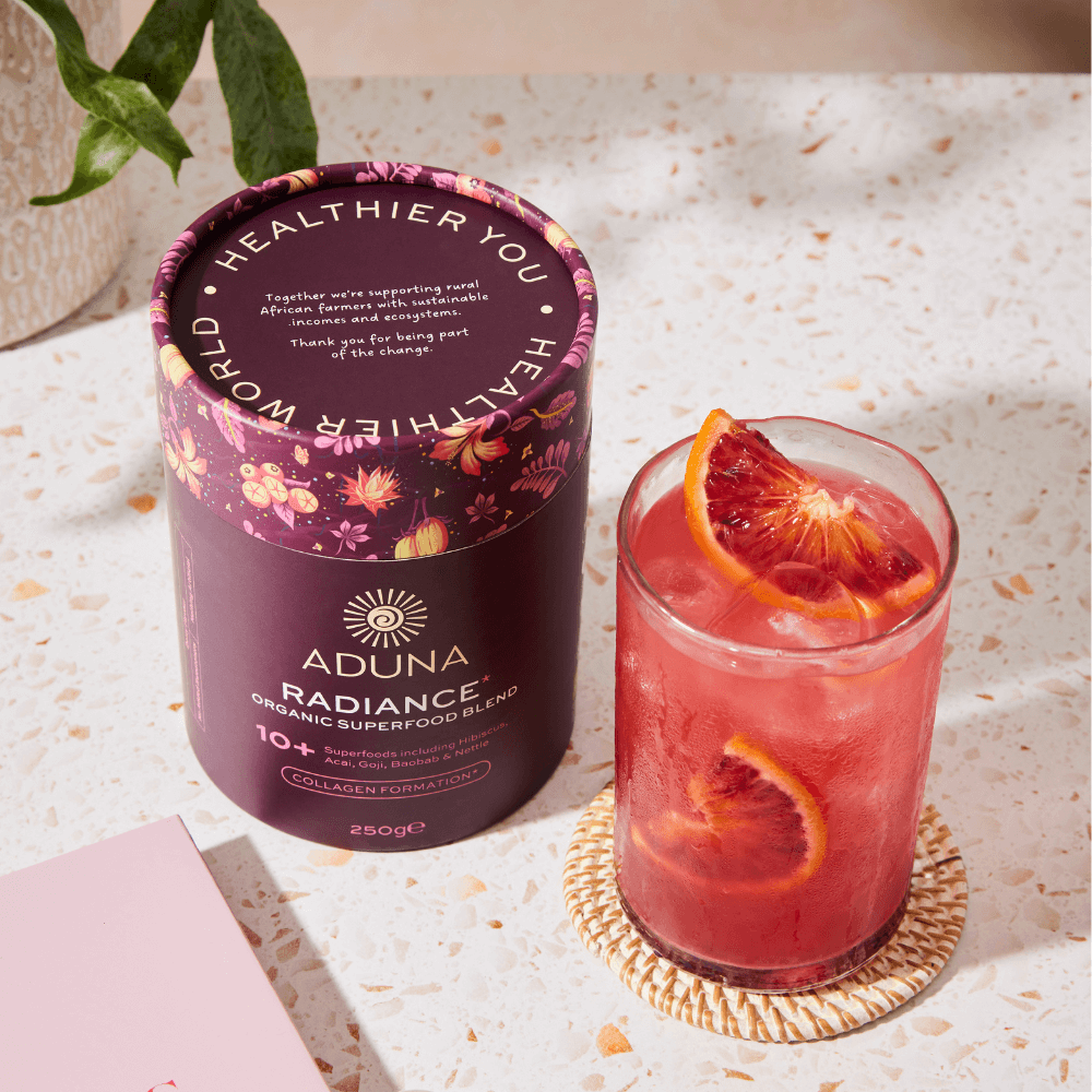 Package of Aduna Radiance Organic Superfood Blend next to a glass of red juice