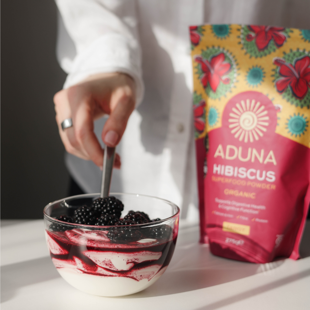 Aduna Hibiscus Superfood Powder 275g package next to a bowl of yoghurt topped with blackberries.