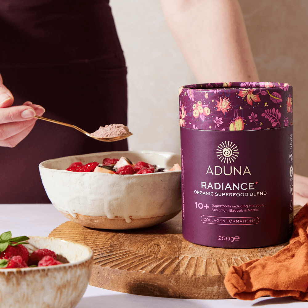 Aduna Radiance Organic Superfood Blend container with a bowl of berries and a spoonful of powder.