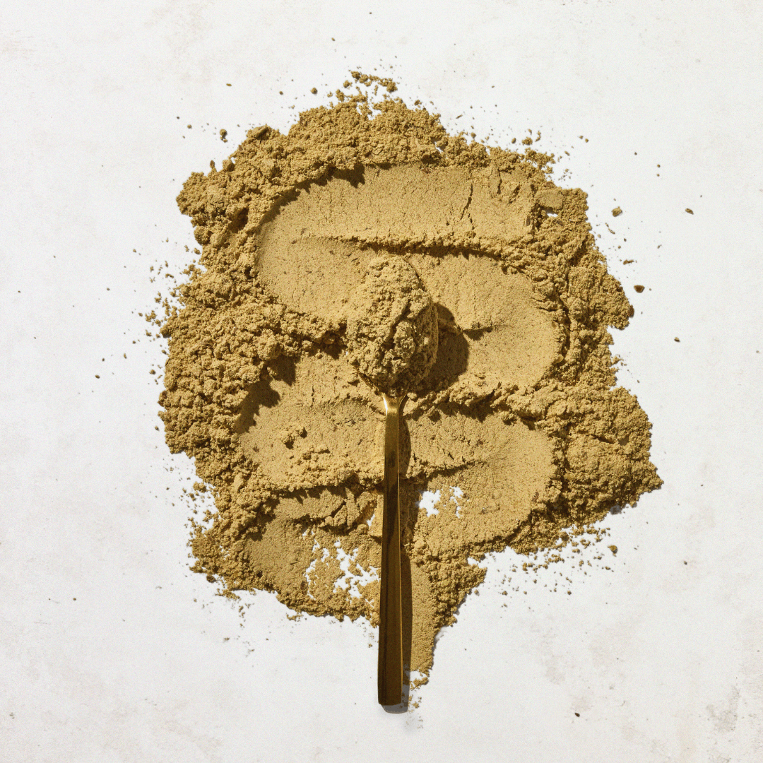 A pile of loose, light brown Aduna Digestion Blend powder spread out with a gold spoon resting on it. The spoon is filled with the same powder.