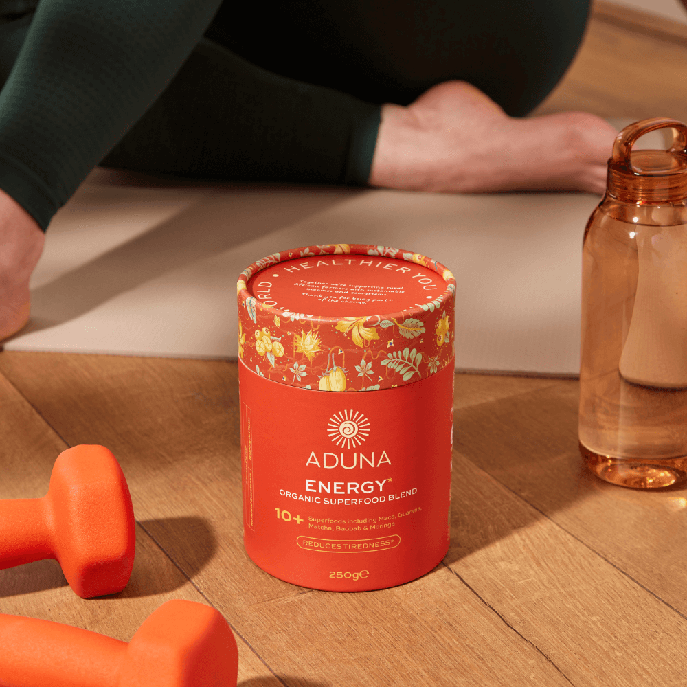 250g cylindrical package of Aduna Energy Organic Superfood Blend on wooden floor