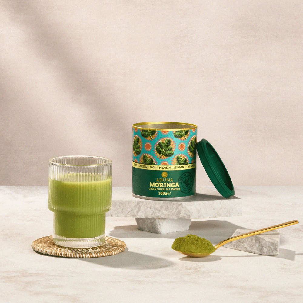 Moringa powder canister with a glass of green juice on a neutral background