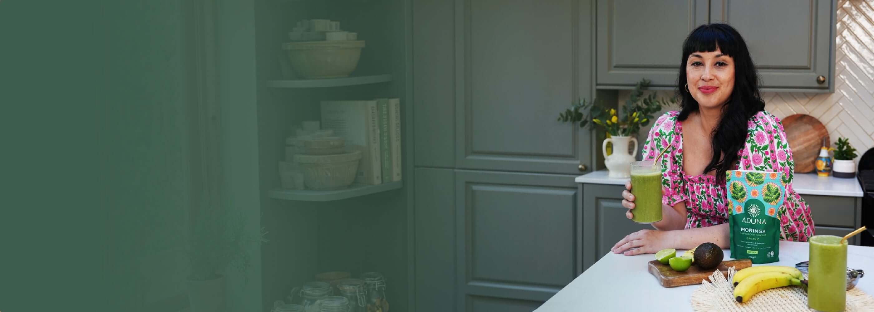 Melissa Hemsley in a kitchen holding a green smoothie with a pouch of Aduna Moringa Powder
