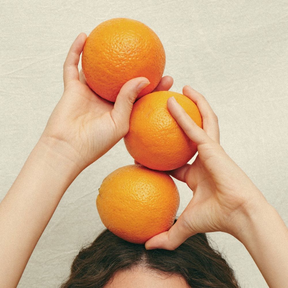 Two hands holding three oranges above their head to represent immunity.