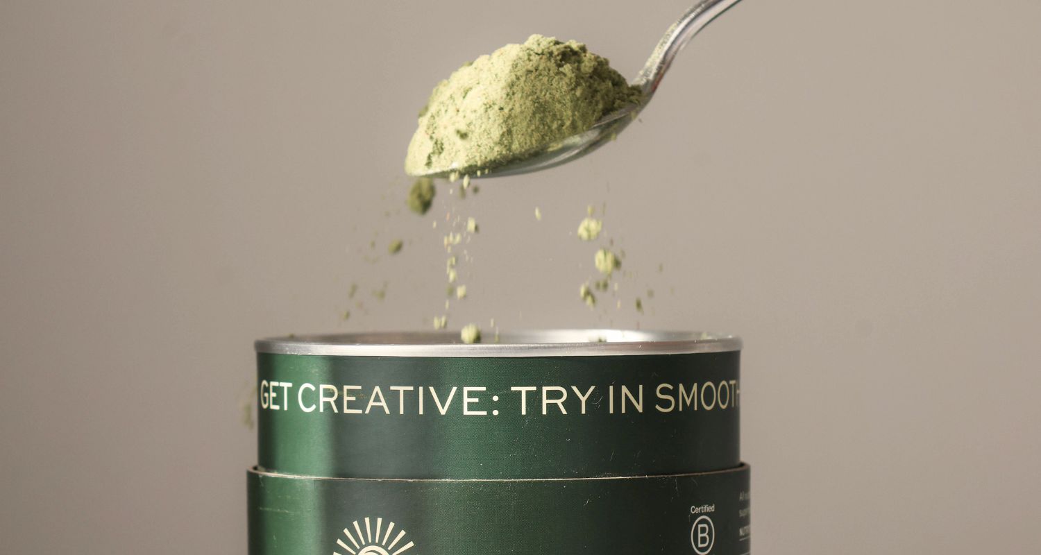 Spoonful of green powder over a container with text on a beige background