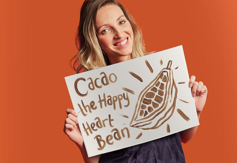 Abigail James holding a sign that says 'Cacao the Happy Heart Bean'