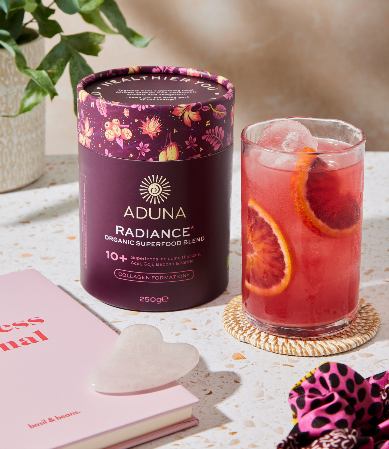 Aduna Radiance organic superfood blend package next to a glass of red juice garnished with slices of orange.