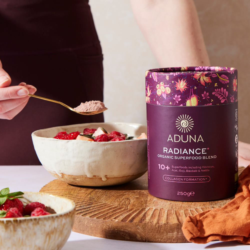 Aduna Radiance Organic Superfood Blend container with a bowl of berries and a spoonful of powder.