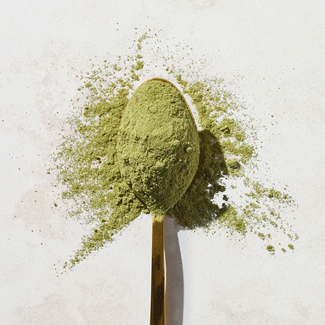 Super Green powder on a gold spoon, viewed from the top down.