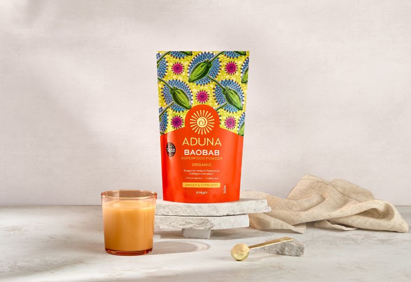 Aduna Baobab packaging with a glass of orange juice.